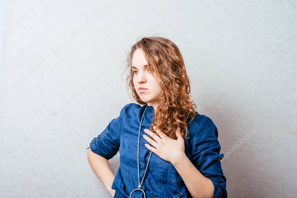 Curly woman holds her hand on his chest, the heart. Gray background.