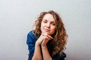 Kıvırcık kız tatlı tatlı gülümser. Gri arkaplan.