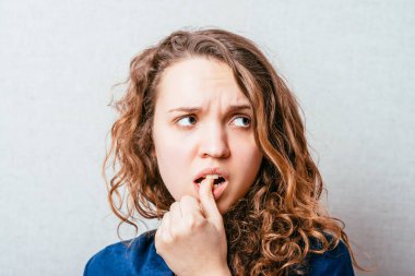 Kıvırcık kız şaşırdı, yüzünün yanında korkmuş eller vardı. Gri arkaplan.