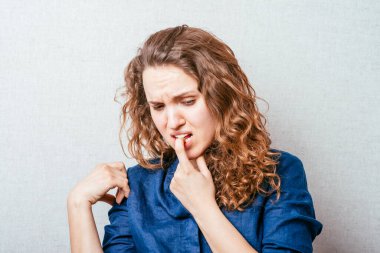 Bir kadın dişinin ağrıdığını düşünerek parmağını ağzına sokuyor. Gri arkaplan