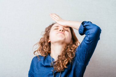 Kıvırcık kız sinirli, öfkeli, eli başının yanında. Gri arkaplan.