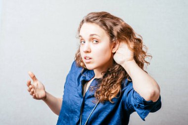 Bir kadın elini kulağının yakınında tutar, duyması zor, yüksek sesle söyler. Gri arkaplan