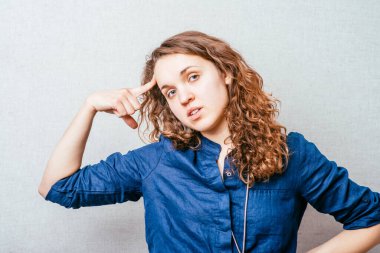 Şakağına parmağını dayayıp düşünen kıvırcık bir kadın. Gri bir arkaplanda.