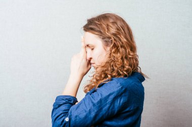 Kıvırcık kız üzgün düşünüyor. Kafasındaki el. Gri arkaplan.