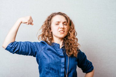 Kolundaki kasları gösteren kıvırcık kadın. Gri bir arkaplanda.