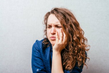 Kıvırcık kız üzgün düşünüyor. Kafasındaki el. Gri arkaplan.