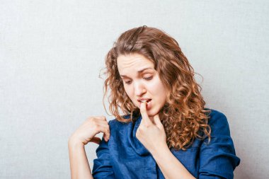 Bir kadın dişinin ağrıdığını düşünerek parmağını ağzına sokuyor. Gri arkaplan