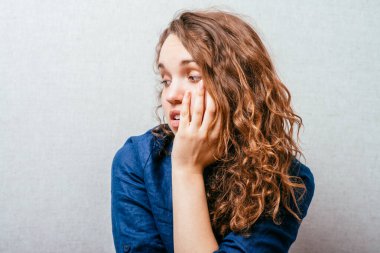 Kıvırcık kız üzgün düşünüyor. Kafasındaki el. Gri arkaplan.