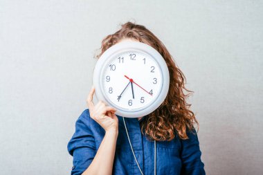 Duvar saati olan kıvırcık kız. Gri arkaplan.