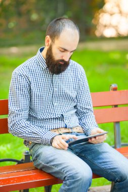 Genç adam parkta dijital tablet kullanıyor.