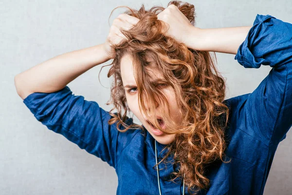 Curly woman tearing his hair. Gray background.