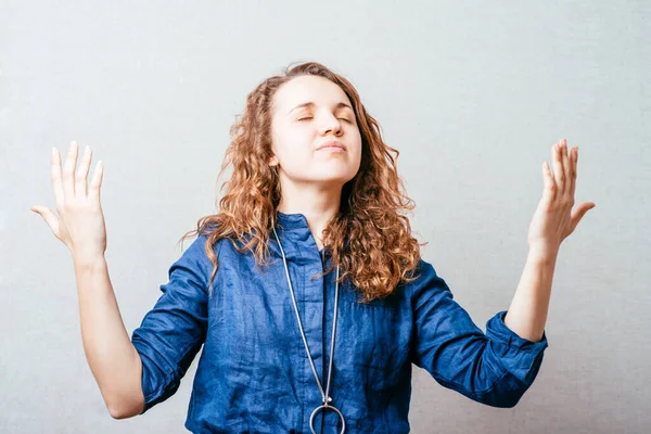 Kıvırcık kız ellerini kaldırıp dua etti. Gri arkaplan.