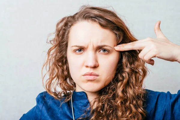 Kıvırcık kız sinirli intiharı, silah şeklindeki bir tapınağa parmağını simüle eder. Gri arkaplan.