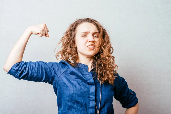 Kolundaki kasları gösteren kıvırcık kadın. Gri bir arkaplanda.