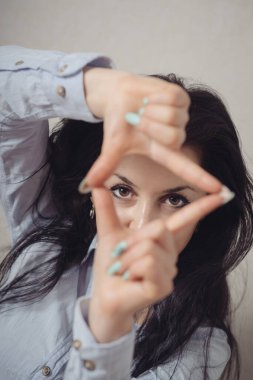 Parmak çerçevesinden bakan bir kadın. Gri bir arkaplanda.