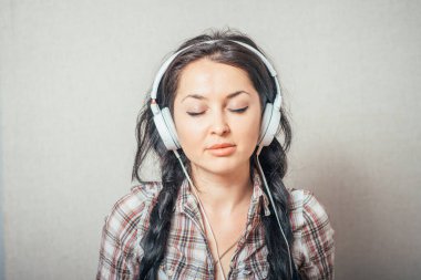 Kulaklıkla müzik dinleyen bir kadın. Gri bir arkaplanda.