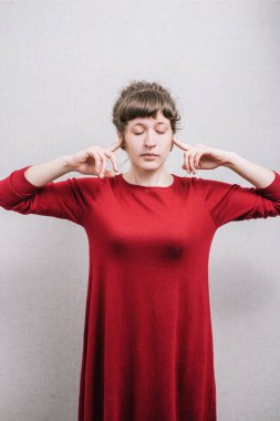 Kulaklarını kapatan bir kadın. Gri bir arkaplanda.