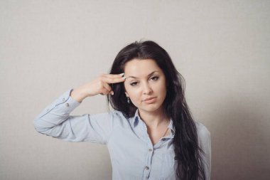 Kadın intihar jesti, şakağına parmak, silah taklidi yapıyor. Gri bir arkaplanda.