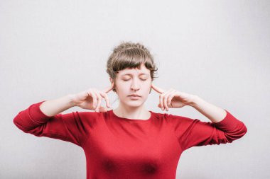 Kulaklarını kapatan bir kadın. Gri bir arkaplanda.