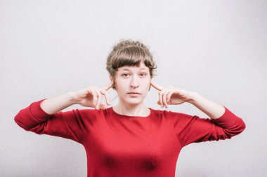 Kulaklarını kapatan bir kadın. Gri bir arkaplanda.