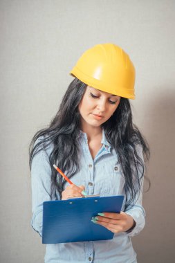 Mühendis kadın gülümsüyor, iş kağıdına yazıyor. sarı koruyucu başlık.