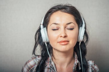 Kulaklıkla müzik dinleyen bir kadın. Gri bir arkaplanda.