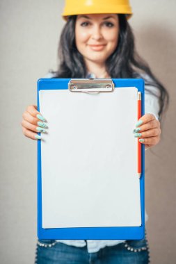 Mühendis kadın gülümsüyor, iş kağıdına yazıyor. sarı koruyucu başlık.