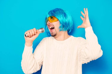 Peruklu ve güneş gözlüklü bir adam mikrofona şarkı söylüyor..