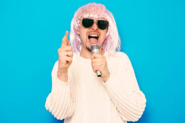 Peruklu ve güneş gözlüklü bir adam mikrofona şarkı söylüyor..