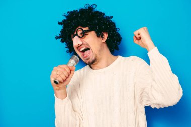 Peruklu ve komik gözlüklü bir adam mikrofona şarkı söylüyor.