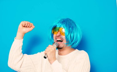 Peruklu ve güneş gözlüklü bir adam mikrofona şarkı söylüyor..