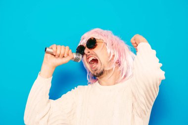 Peruklu ve güneş gözlüklü bir adam mikrofona şarkı söylüyor..