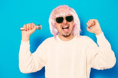 Peruklu ve güneş gözlüklü bir adam mikrofona şarkı söylüyor..