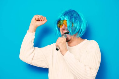 Peruklu ve güneş gözlüklü bir adam mikrofona şarkı söylüyor..