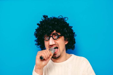 Peruklu ve komik gözlüklü bir adam mikrofona şarkı söylüyor.