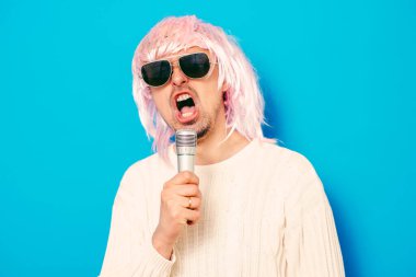 Peruklu ve güneş gözlüklü bir adam mikrofona şarkı söylüyor..