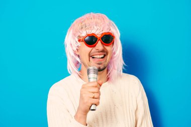 Peruklu ve güneş gözlüklü bir adam mikrofona şarkı söylüyor..