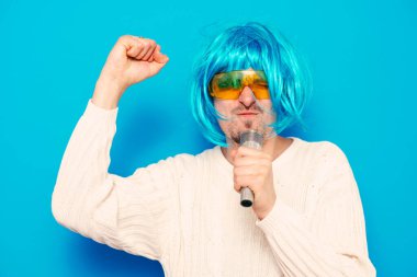 Peruklu ve güneş gözlüklü bir adam mikrofona şarkı söylüyor..