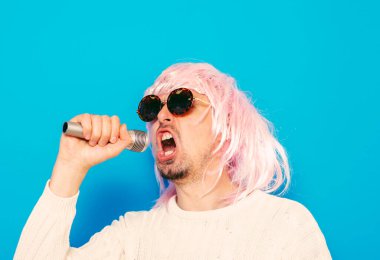 Peruklu ve güneş gözlüklü bir adam mikrofona şarkı söylüyor..