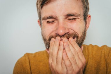 Adam gülüyor ve ağzını kapatıyor.