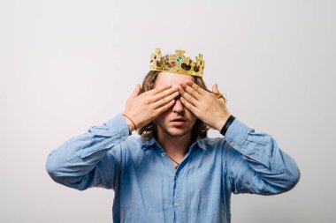 Taç giymiş, elleri kapalı gözleri olan adam.