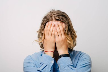 Adam elleriyle gözlerini kapadı. Gri bir arkaplanda.