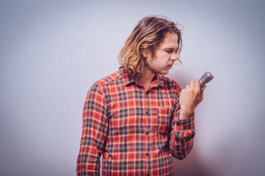 Yakışıklı adam mikrofona şarkı söylüyor. Çekici bir adamın duygusal portresi. Gri bir arka plan.