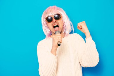 Peruklu ve güneş gözlüklü bir adam mikrofona şarkı söylüyor..