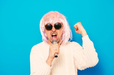 Peruklu ve güneş gözlüklü bir adam mikrofona şarkı söylüyor..