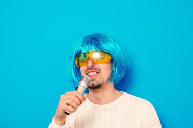 Peruklu ve güneş gözlüklü bir adam mikrofona şarkı söylüyor..