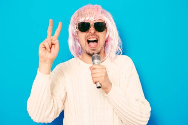 Peruklu ve güneş gözlüklü bir adam mikrofona şarkı söylüyor..