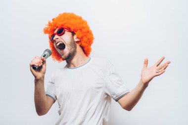 Peruklu ve güneş gözlüklü bir adam mikrofona şarkı söylüyor..