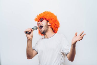 Peruklu ve güneş gözlüklü bir adam mikrofona şarkı söylüyor..