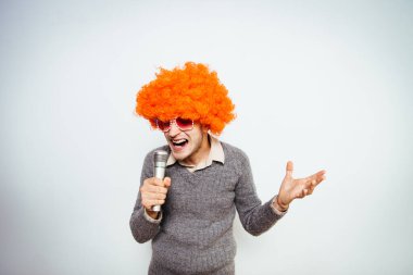 Peruklu ve güneş gözlüklü bir adam mikrofona şarkı söylüyor..